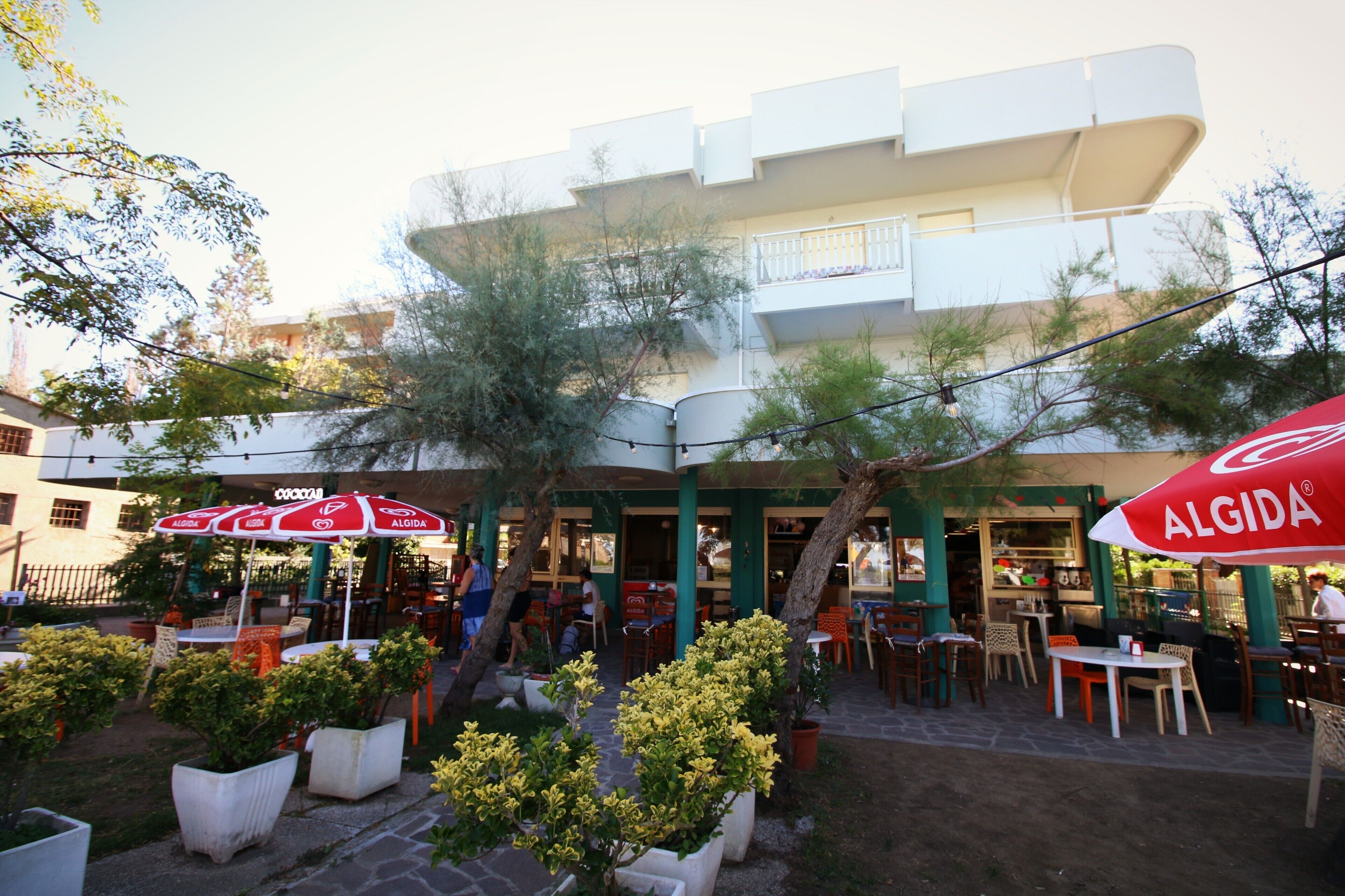 Zona de café al aire libre con mesas y sillas, rodeada de macetas y sombrillas.