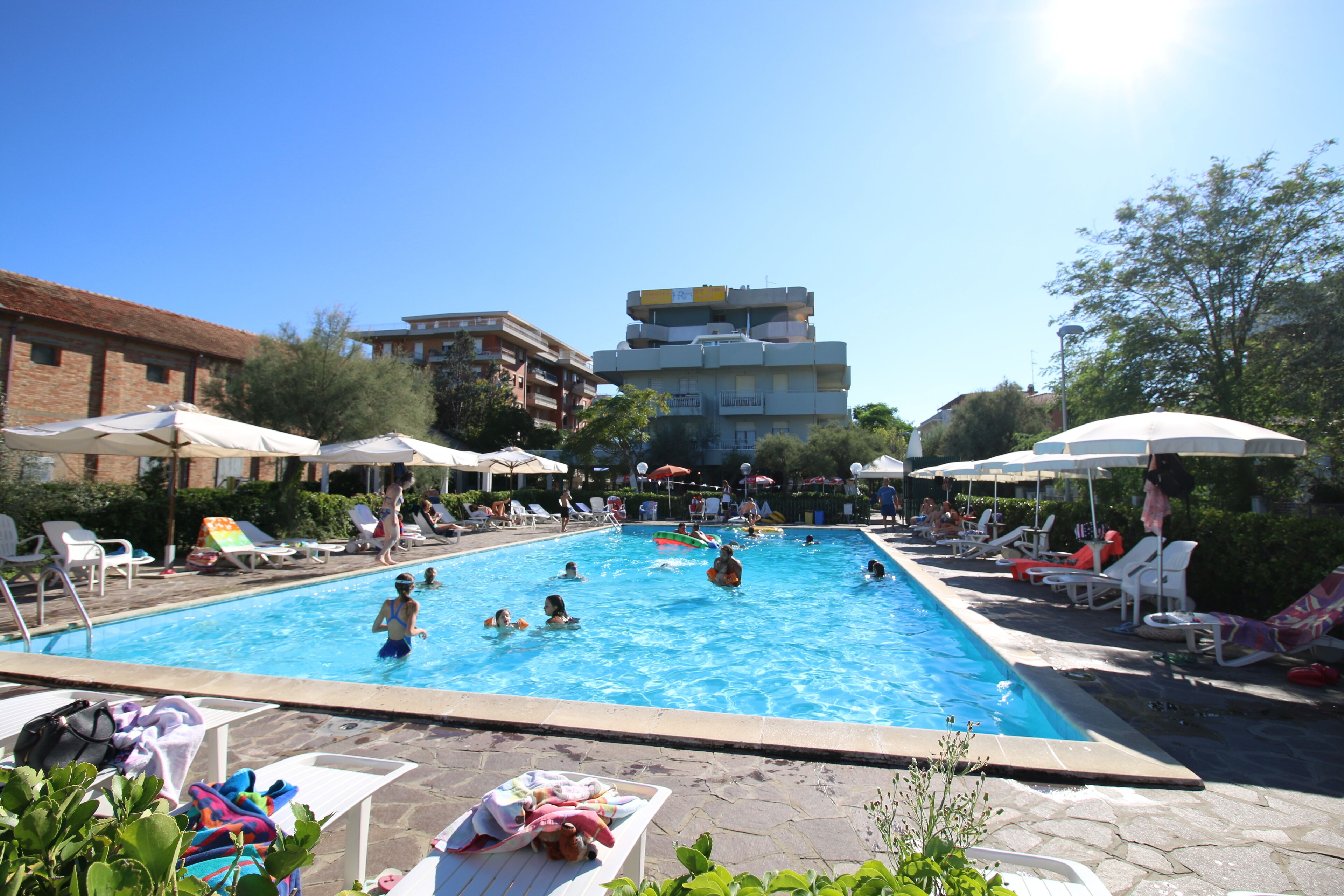 Una piscina con sillas de descanso y sombrillas, rodeada de edificios.