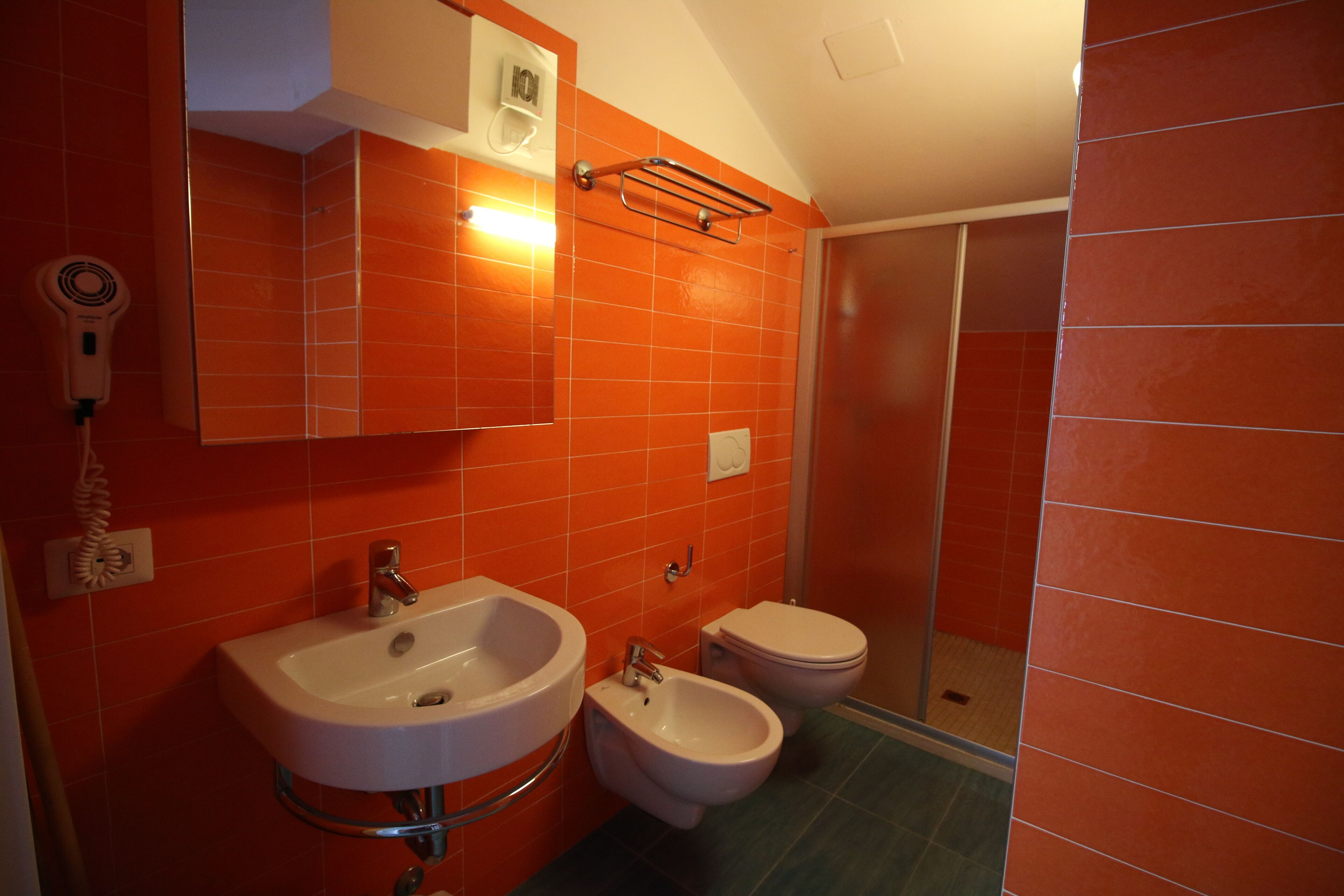 A bathroom with a sink, bidet, and toilet, all in a red-tiled room.