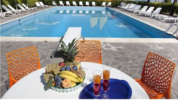 A poolside setting with a table set for two, featuring a fruit bowl and two glasses of juice. - Hotel Residenza Giardino (Bellaria-Igea Marina)