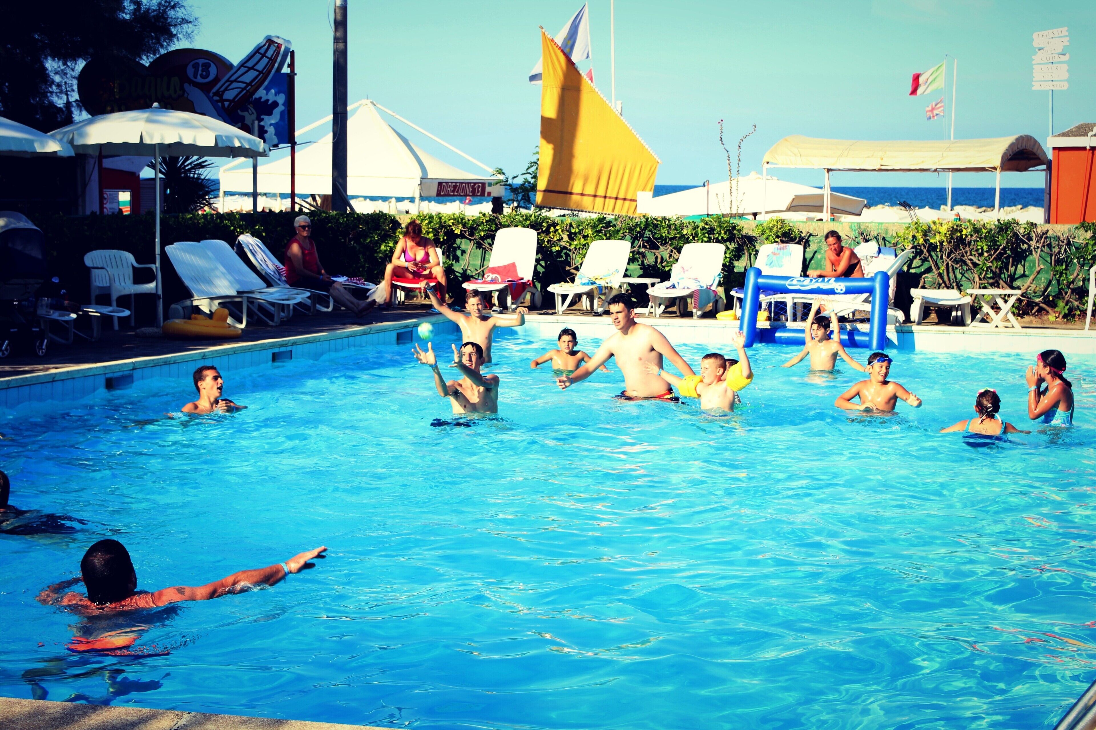 A swimming pool with people enjoying the water, surrounded by lounge chairs and umbrellas.
