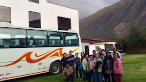 A group of people posing in front of a white bus with orange and black designs, parked in front of a building with a mountain in the background. - Casa San Vicente Yucay (Yucay)