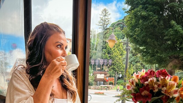 A dining table with a glass of orange juice, a plate with pastries, and a vase with flowers. - Hotel Vovó Carolina (Gramado)