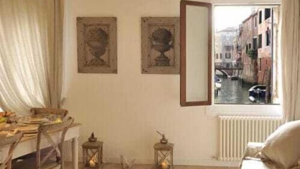 Una habitación con techo de madera, una cama, una mesa con sillas, un ventanal con vistas a edificios y dos cuadros enmarcados en la pared.