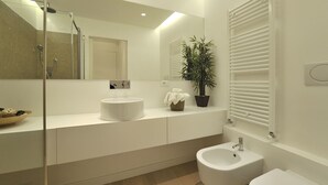 Un baño moderno con un espejo grande, un lavabo redondo, un bidé y una planta en maceta.