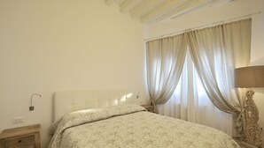 Un dormitorio con una cama, una mesita de noche, una lámpara y una ventana con cortinas.