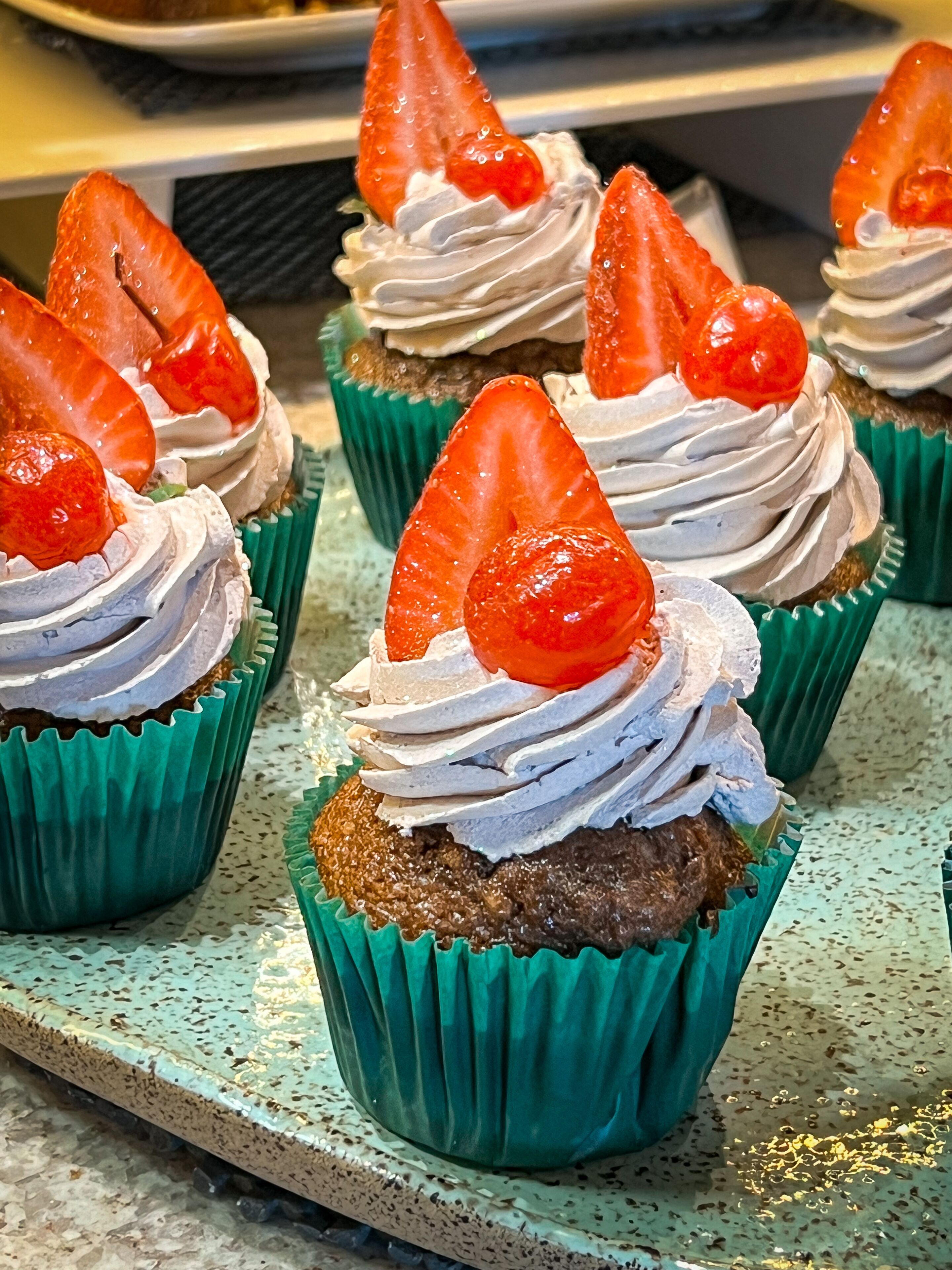 Cupcakes with whipped cream and strawberries on a tray.