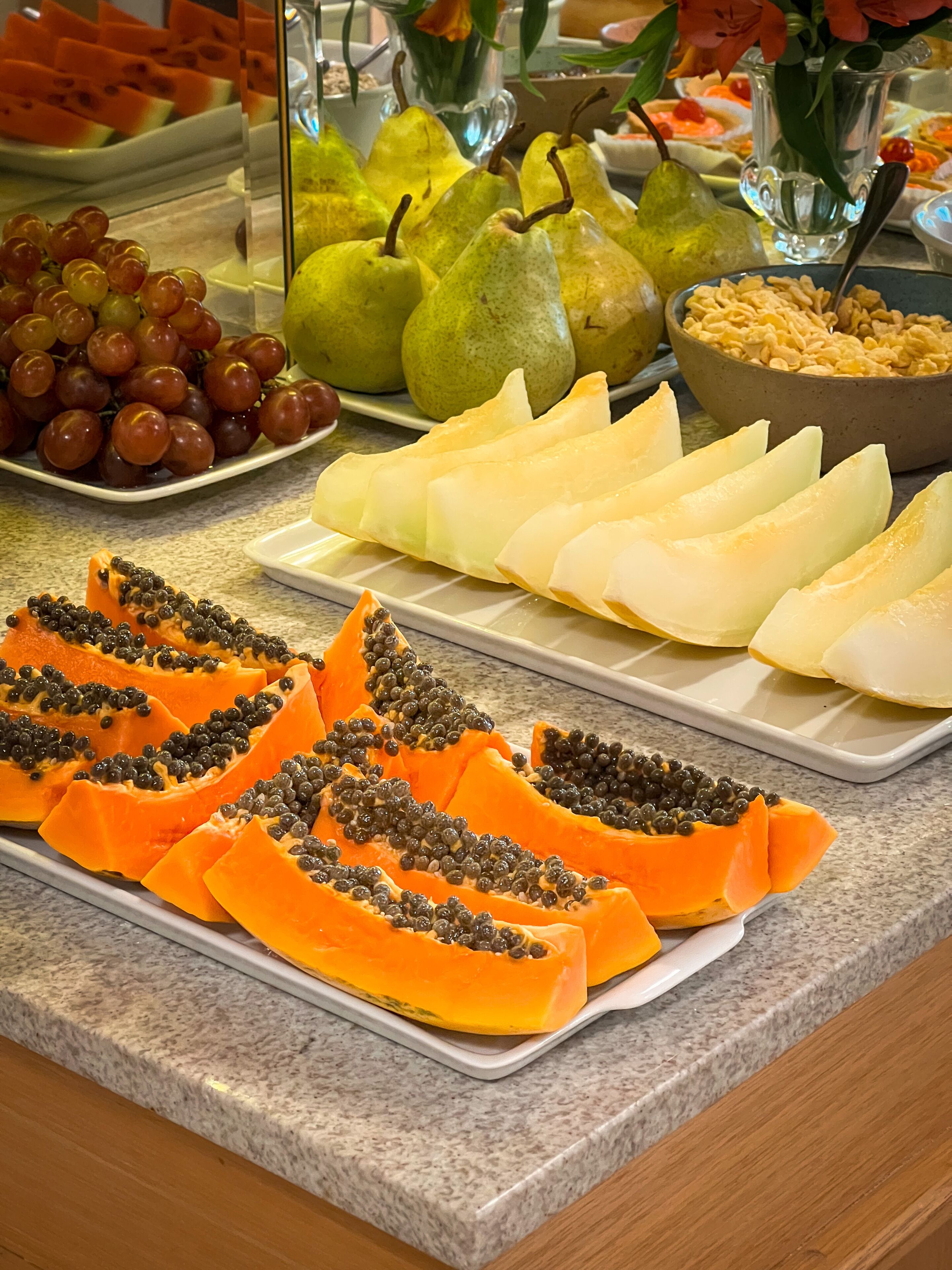 A buffet with various fruits and vegetables, including grapes, pears, and papaya.