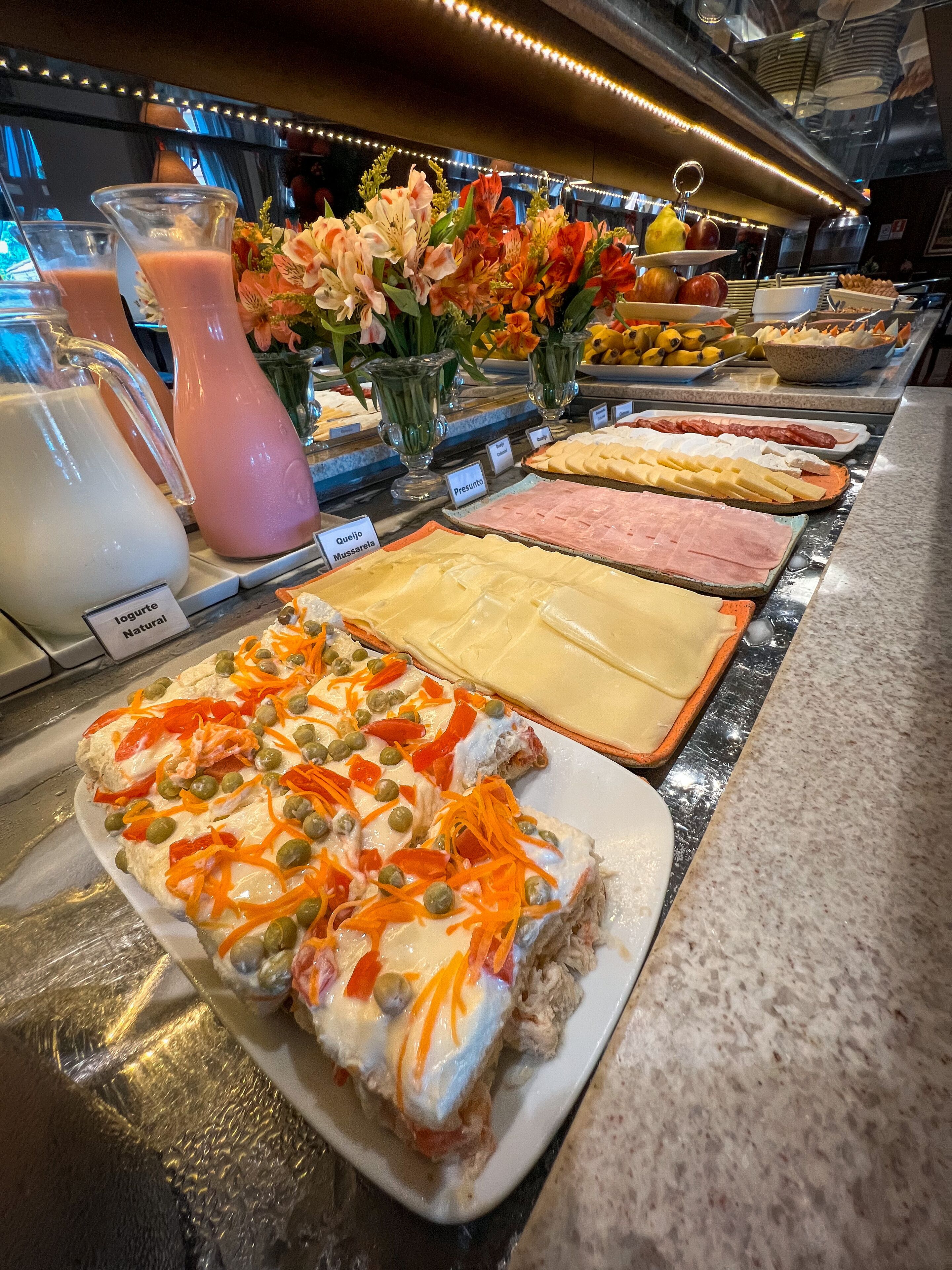 Un buffet proposant une variété de plats, notamment des fromages, des viandes et une salade composée de carottes et de petits pois.