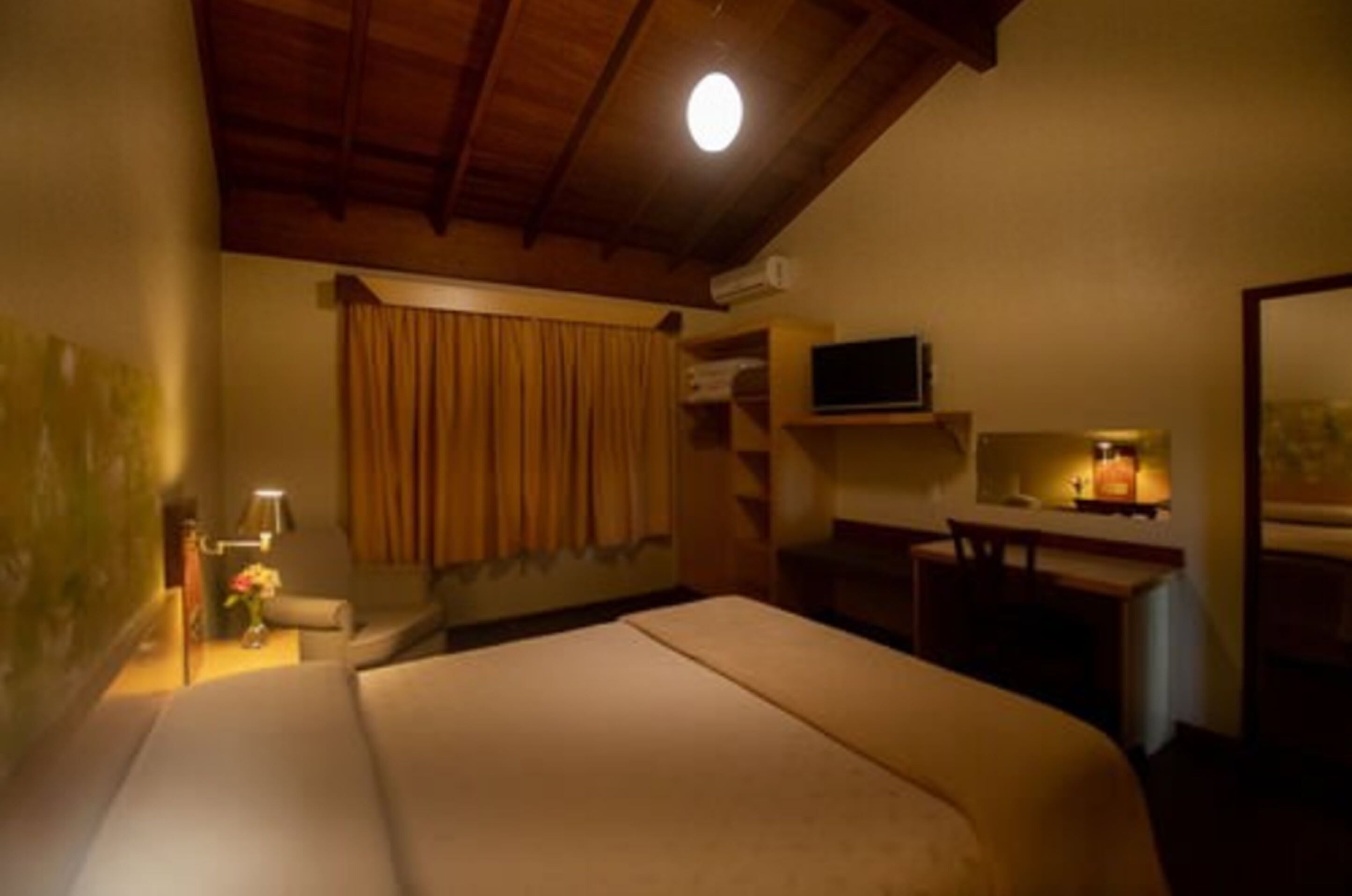 Una camera d'albergo con un letto, una scrivania, una televisione e una finestra con tende.