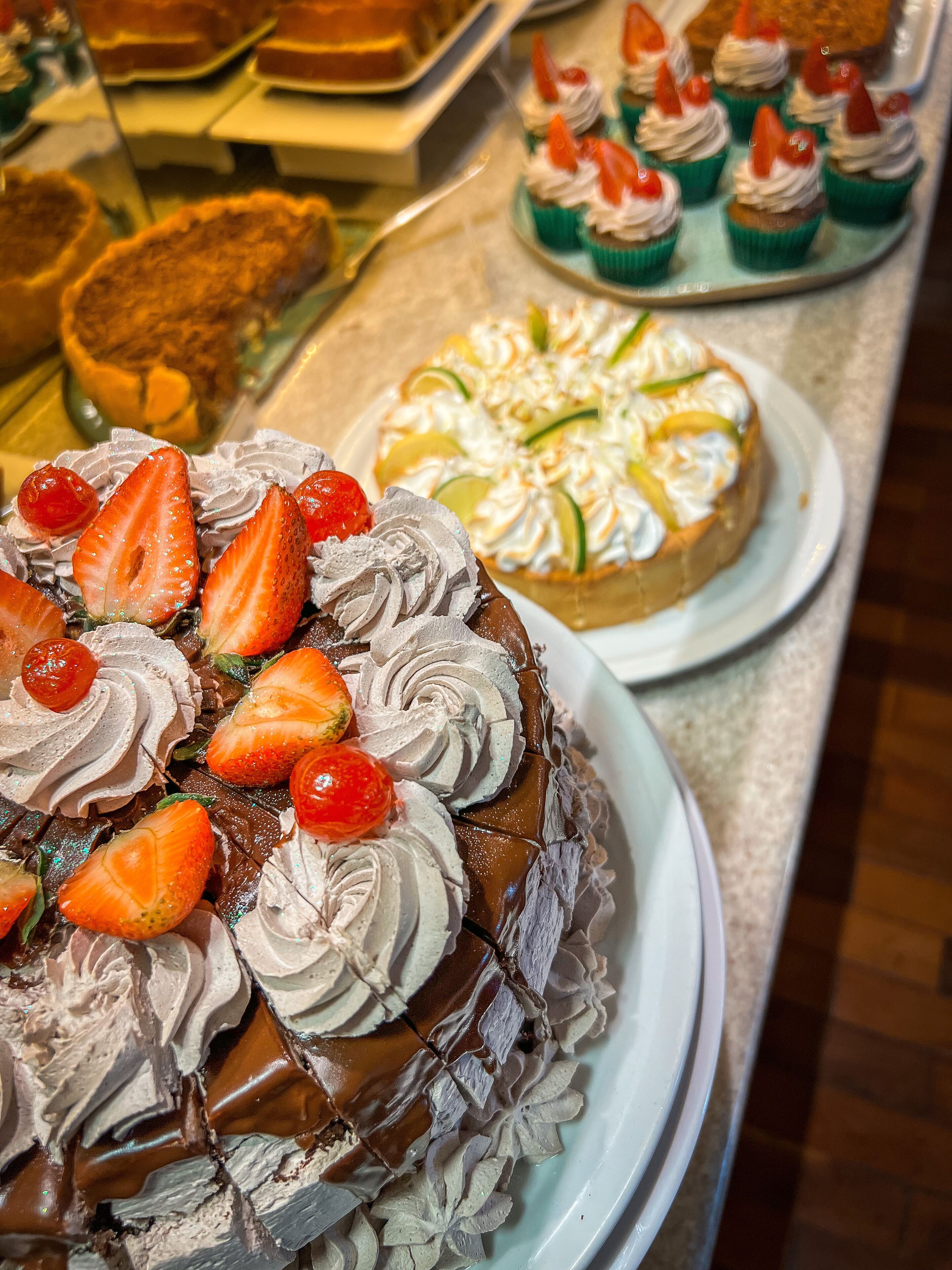 Un assortiment de desserts comprenant un gâteau au chocolat aux fraises et à la crème fouettée, une tarte aux fruits agrémentée de tranches de citron vert, et plusieurs petits gâteaux aux fraises.
