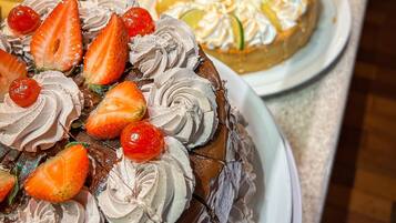 Un assortiment de desserts comprenant un gâteau au chocolat aux fraises et à la crème fouettée, une tarte aux fruits agrémentée de tranches de citron vert, et plusieurs petits gâteaux aux fraises.