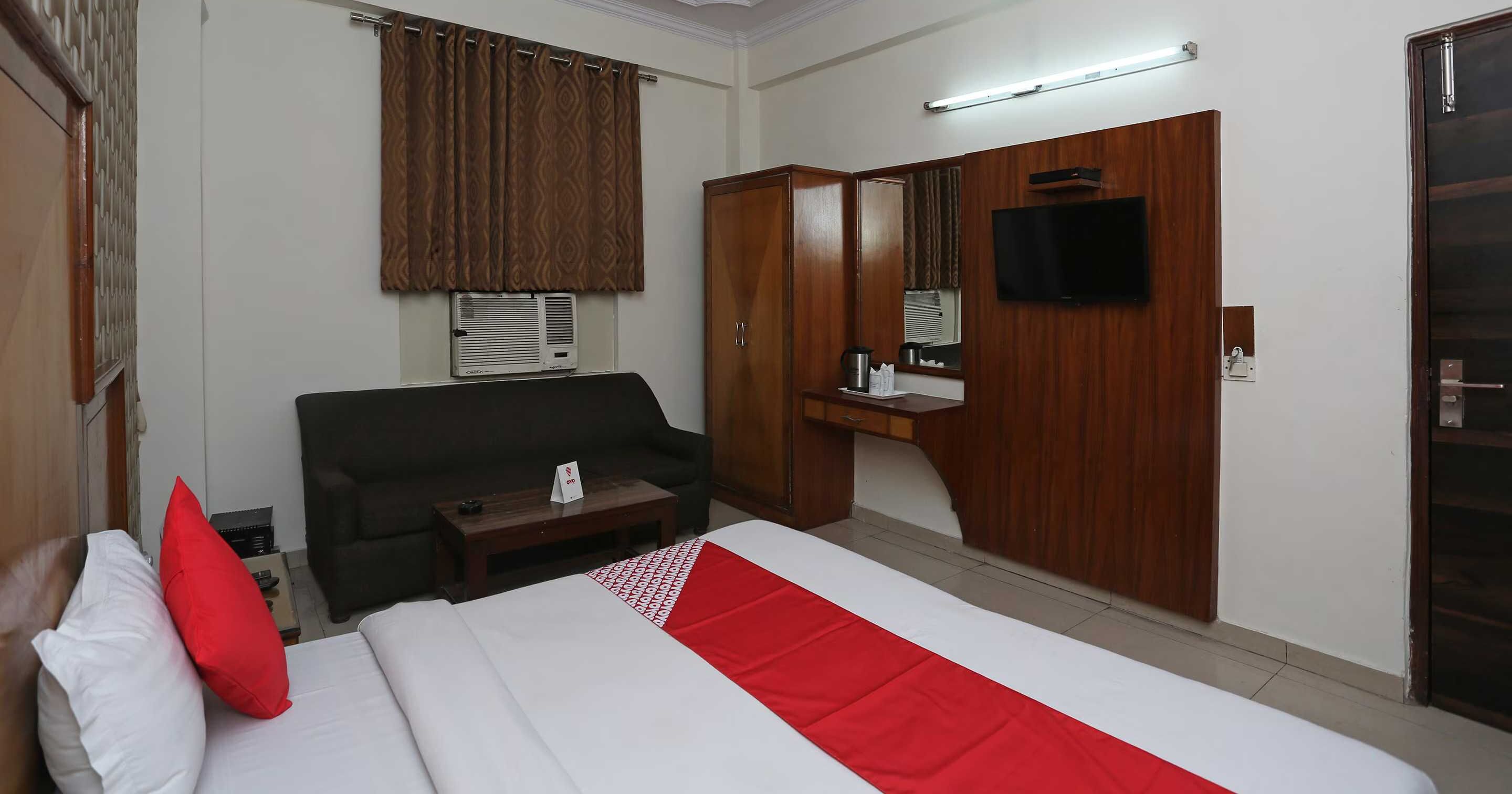 Habitació d'hotel amb un llit, un sofà, una taula petita, un mirall, una televisió i un armari.