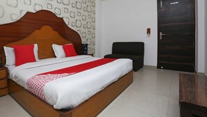Una cama bien hecha con un cabecero de madera, una mesita de noche con un teléfono y una silla en una habitación con un papel tapiz estampado y una puerta oscura.