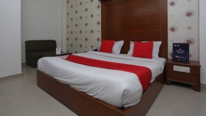 Habitación de hotel con una cama grande, un cabecero de madera, una mesita de noche con lámpara y una silla.