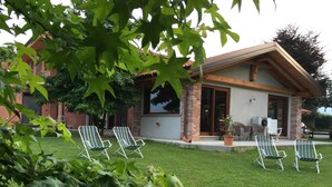 A house with a brick exterior, a covered patio area with four striped lawn chairs, and a well-maintained lawn. - Agriturismo La Virginia (Revello)