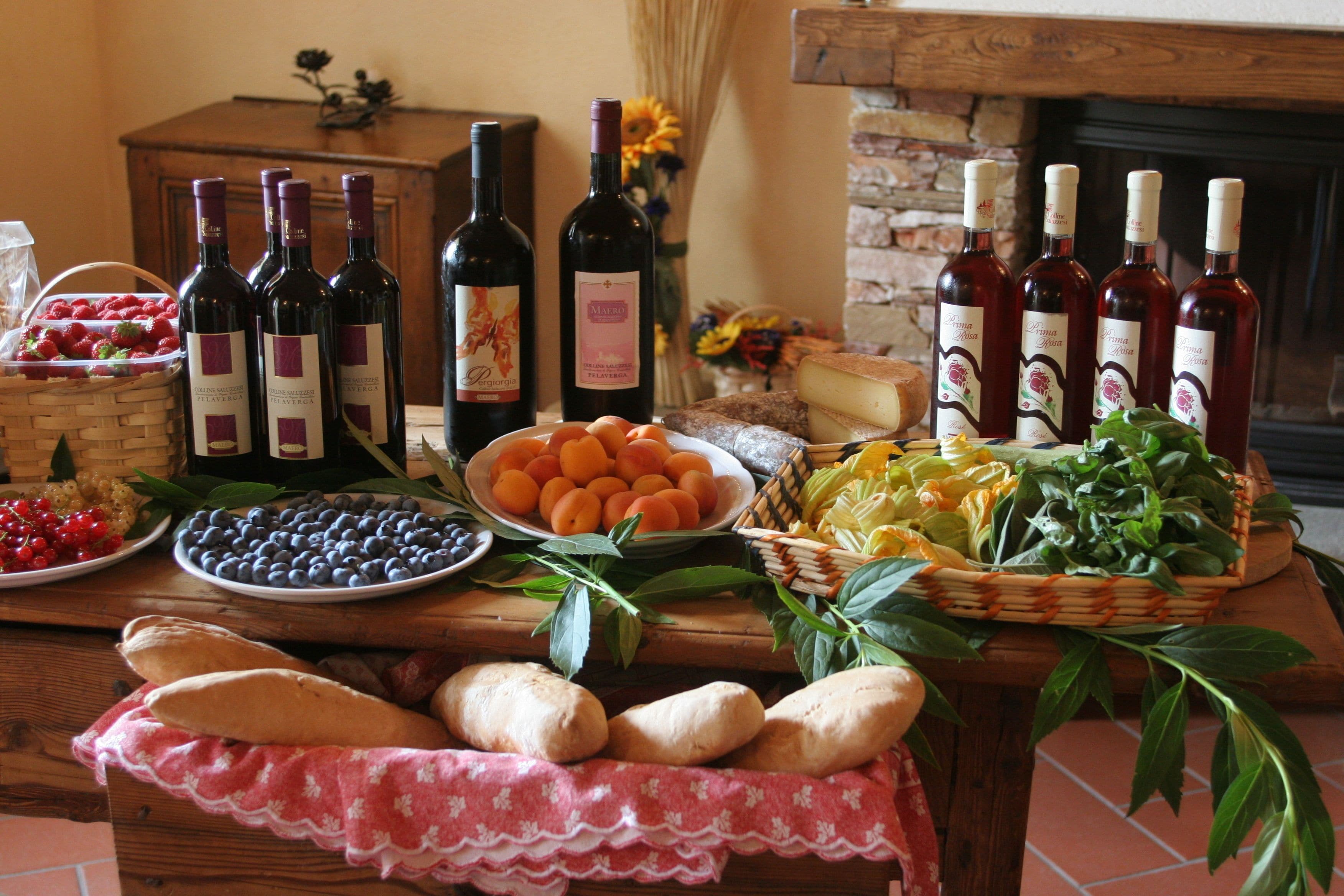 A wooden table with various food items, including bread, fruits, and cheese, and several bottles of wine.