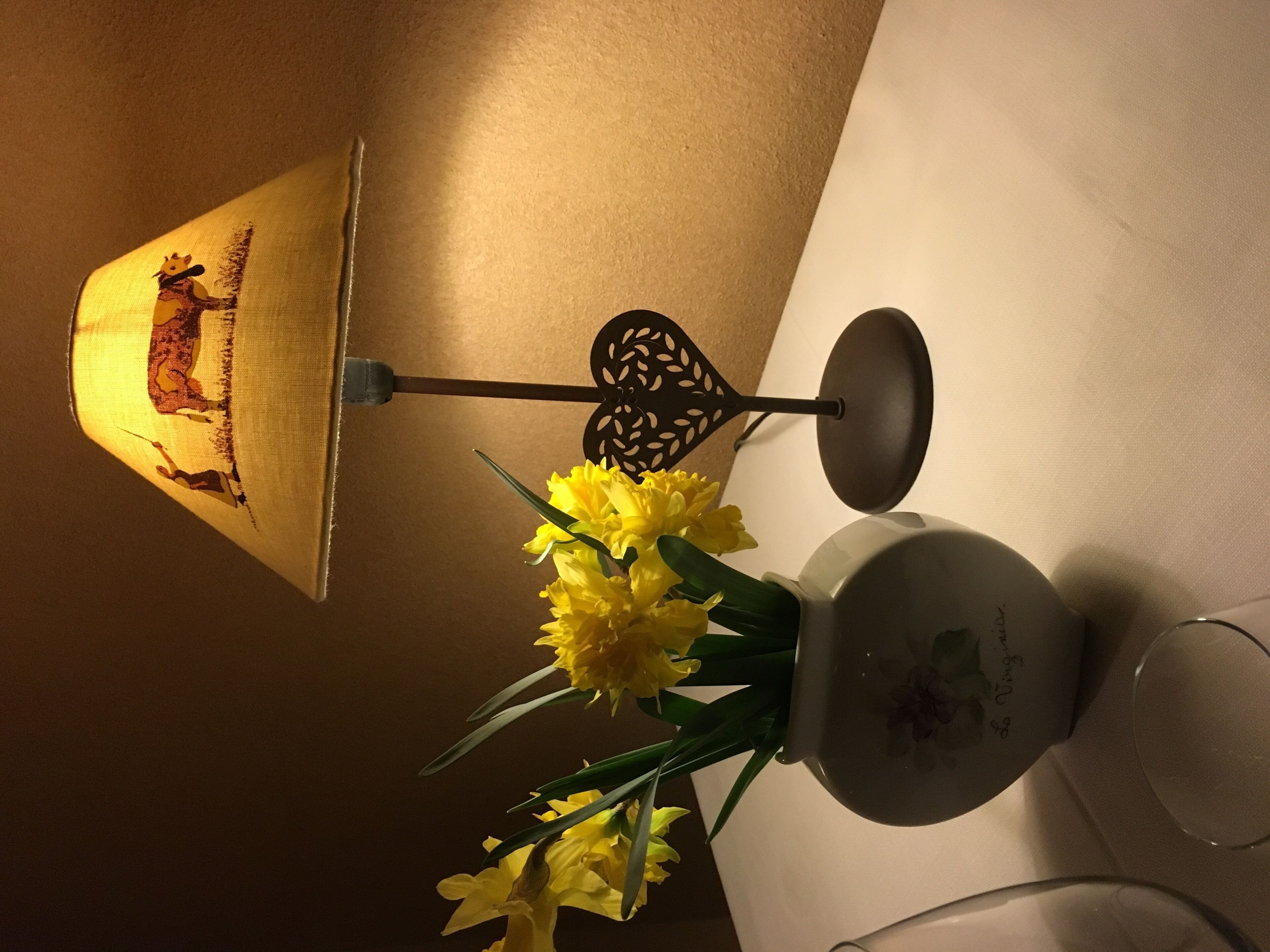 Una lampada con paralume decorativo, un lampadario a parete e un vaso con fiori gialli su un tavolo.