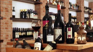 A wooden wine rack with various bottles and a glass of red wine. - Agriturismo La Virginia (Revello)