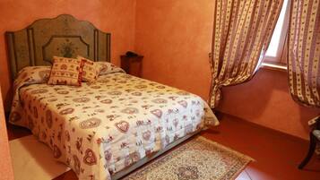 Ein Schlafzimmer mit Bett, gemusterten Textilien, einem Kopfteil, einem Nachttisch, einem Teppich und Vorhängen.