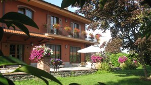 A two-story building with a balcony, surrounded by a well-maintained garden with various flowering plants. - Agriturismo La Virginia (Revello)
