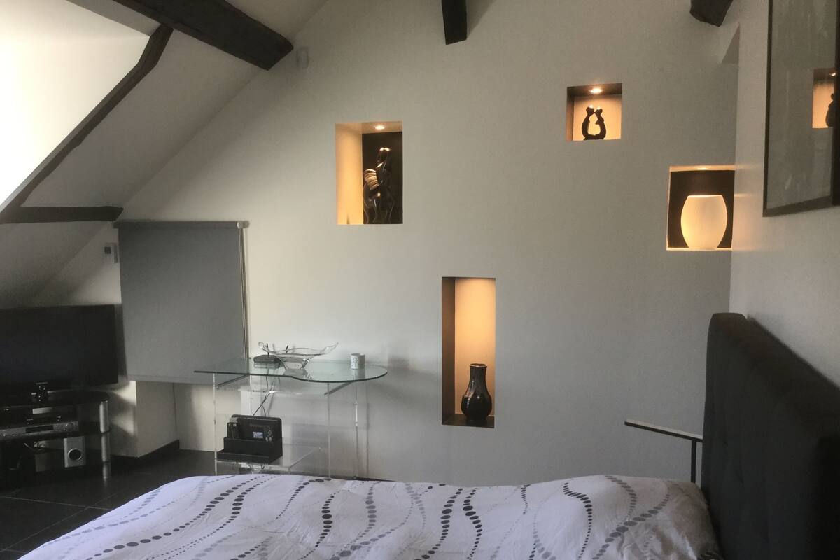 A bedroom with a bed, a desk, and a TV. There are wall-mounted shelves with decorative items.
