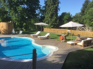 Um quintal com piscina, deck de madeira, cadeiras de lounge e guarda-sóis.