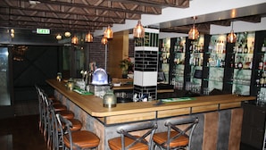 Een bar met een houten toonbank, barstoelen, hangende koperen hanglampen en een betegelde achterwand.