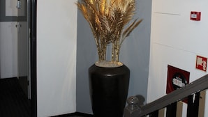 Een hal met een grote potplant, een trap en een rookmelder aan de muur.