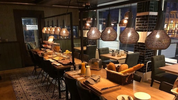 Een restaurant met meerdere tafels, elk gedekt met borden, bestek en brood.