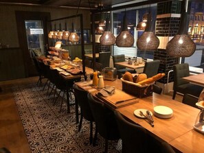 A restaurant with multiple tables, each set with plates, cutlery, and bread.