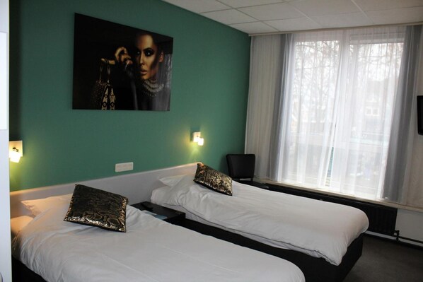 A hotel room with two beds, a large window with sheer curtains, a painting on the wall, and a chair.