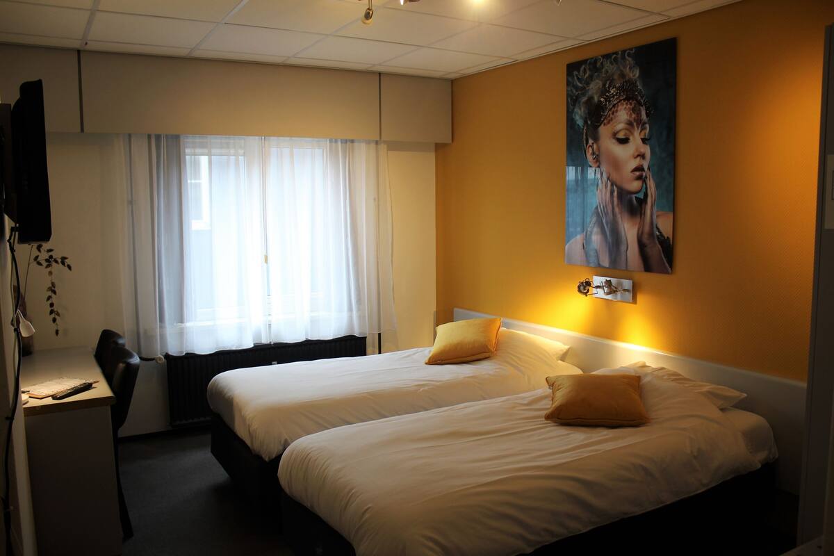 A hotel room with two beds, a desk, and a large window with curtains.