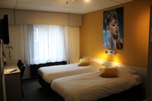 A hotel room with two beds, a desk, and a large window with curtains.