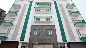 A multi-story building with a modern architectural design, featuring balconies and a central entrance with a glass door. - Capital O 14043 Hotel Star Holiday (Chennai)
