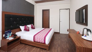 A hotel room with a large bed, wooden headboard, a flat-screen TV mounted on the wall, a desk with a coffee maker, and a door leading to another room. - Capital O 14043 Hotel Star Holiday (Chennai)