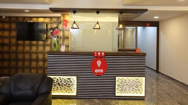 A reception desk with a modern design, featuring a logo, a clock, and a sign indicating the current time. - Capital O 14043 Hotel Star Holiday (Chennai)