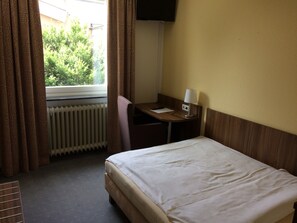 Een hotelkamer met een bed, een bureau, een stoel, een lamp en een raam met gordijnen.