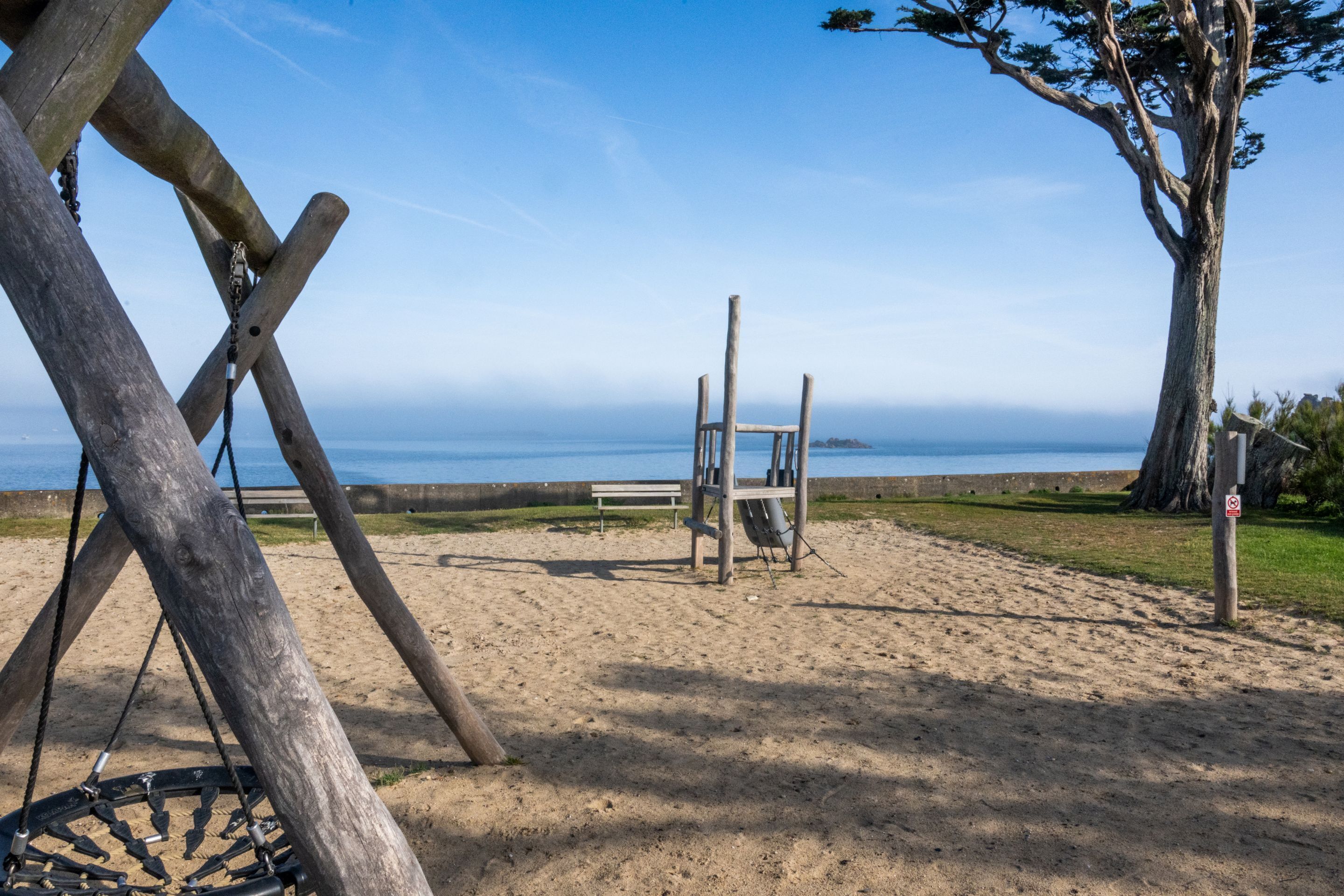 A beach with a swing set, a wooden bench, and a lifeguard tower.