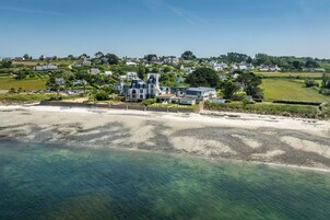 A coastal property with a large house, a beach, and surrounding greenery.