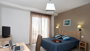 Une chambre d’hôtel comprenant un lit, un bureau avec un ordinateur portable, une chaise, une télévision et une fenêtre avec des rideaux.