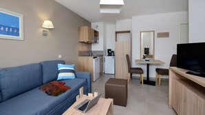 Un salon moderne comprenant un canapé, une table basse, un téléviseur, un coin repas avec une table et des chaises, un coin cuisine avec un réfrigérateur et un four à micro-ondes, et une salle de bain avec un miroir et un porte-serviettes.