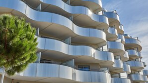 Un bâtiment moderne doté de balcons incurvés et d’un pin qui se trouve devant.