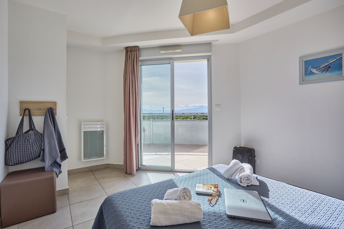 Ein Hotelzimmer mit Bett, Laptop, Koffer, Handtasche und Blick ins Freie.