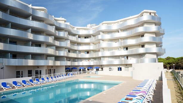 Un hôtel moderne doté d’une piscine, de nombreux balcons et de chaises longues.