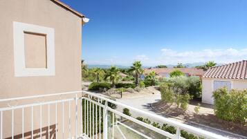 Un balcón con vistas a una zona residencial, que incluye casas con tejados rojos y palmeras.
