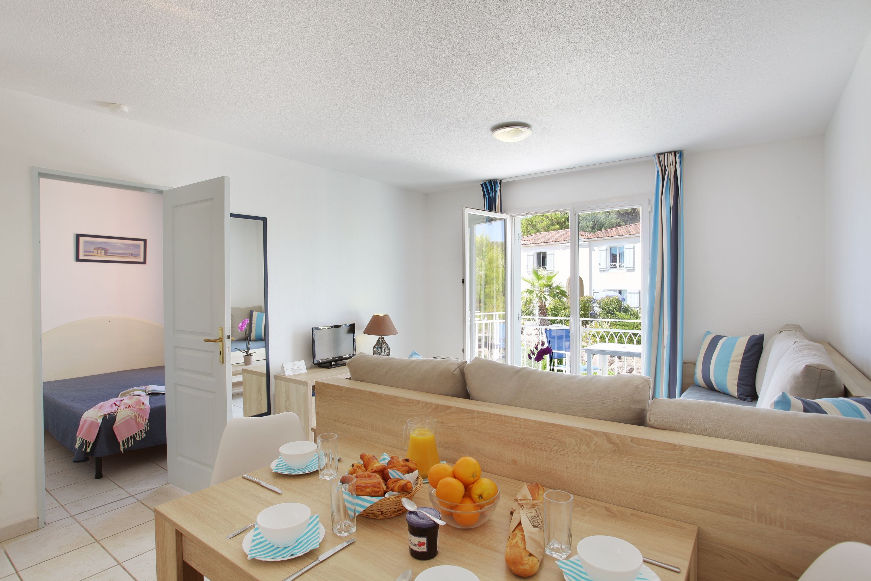 A modern living room with a sofa, a dining table with breakfast items, and a bed in the background.
