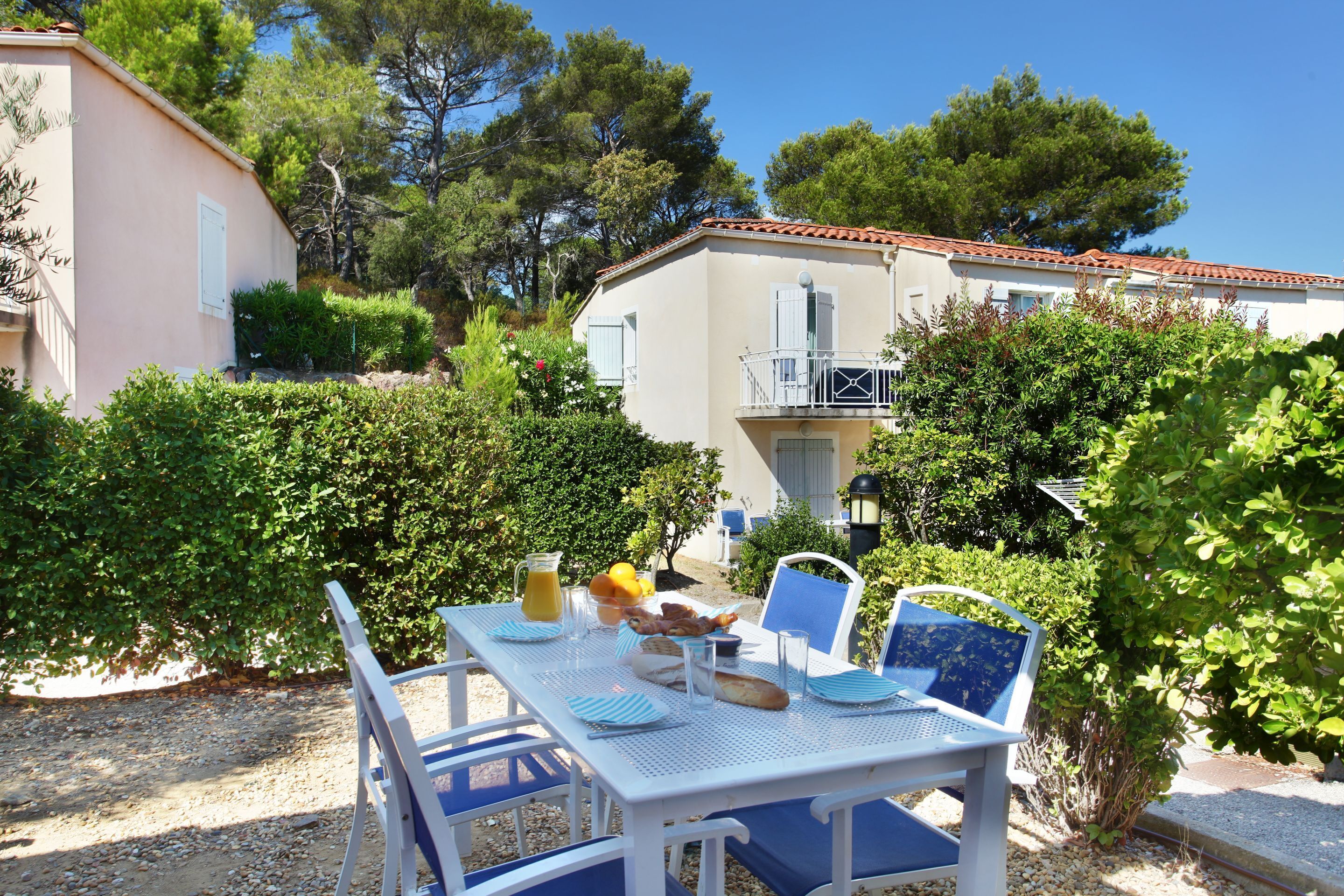 An outdoor dining area with a table set for breakfast, surrounded by greenery and buildings.