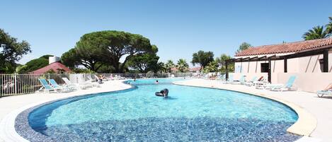 A large, clear swimming pool with lounge chairs and a covered area.