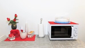 A white microwave with a red top, a vase with red roses, a stack of red napkins, a tissue roll, and a small box on a red mat. - Terrazze Italiane City Center (Verona)